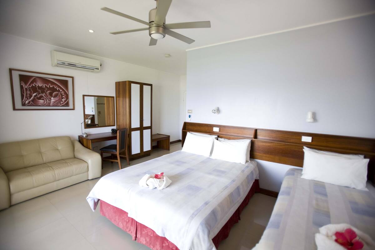 A hotel room with a bed, a sofa, a desk, and a ceiling fan.