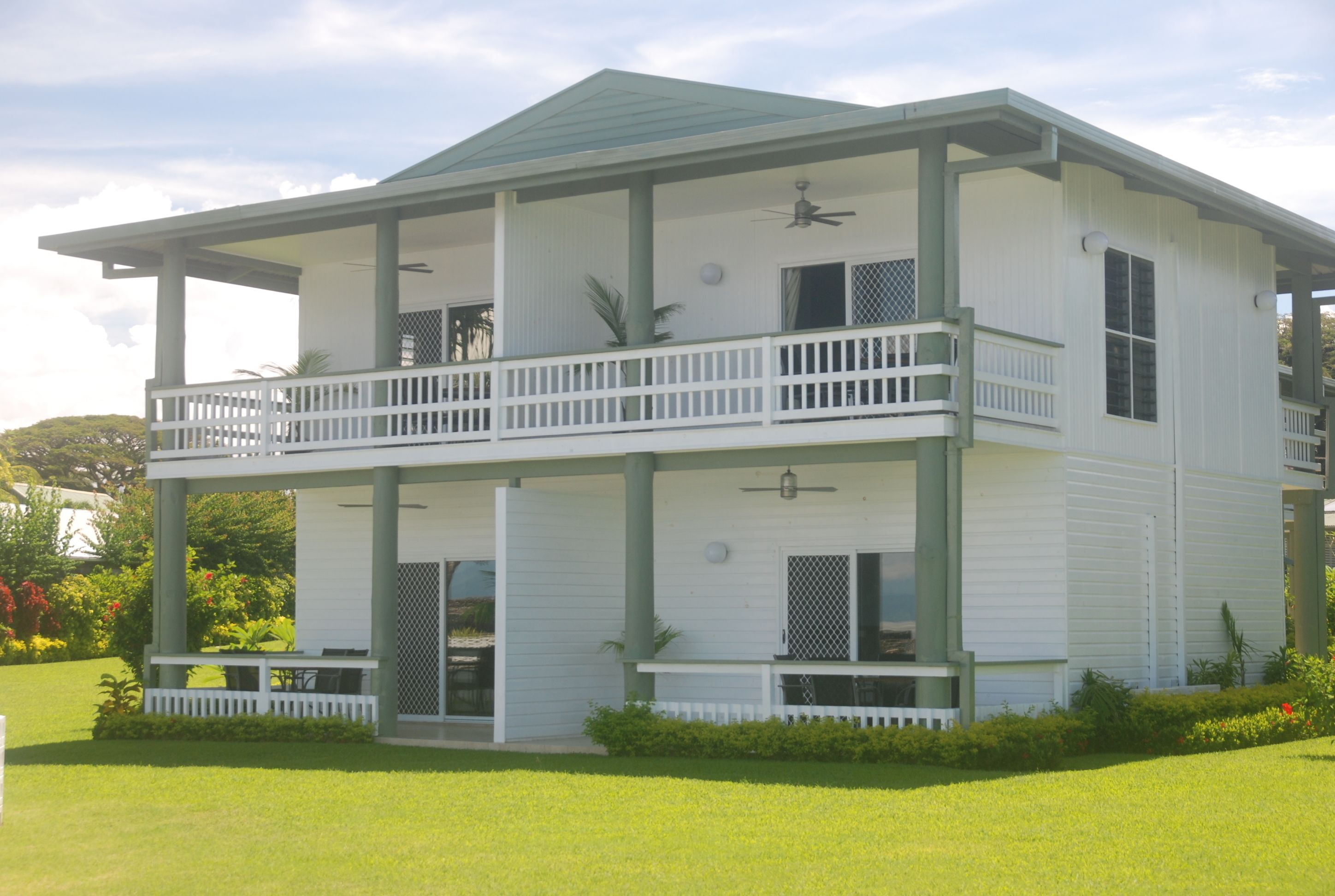 A two-story house with a balcony on the upper floor, a covered porch on the ground floor, and a well-maintained lawn.