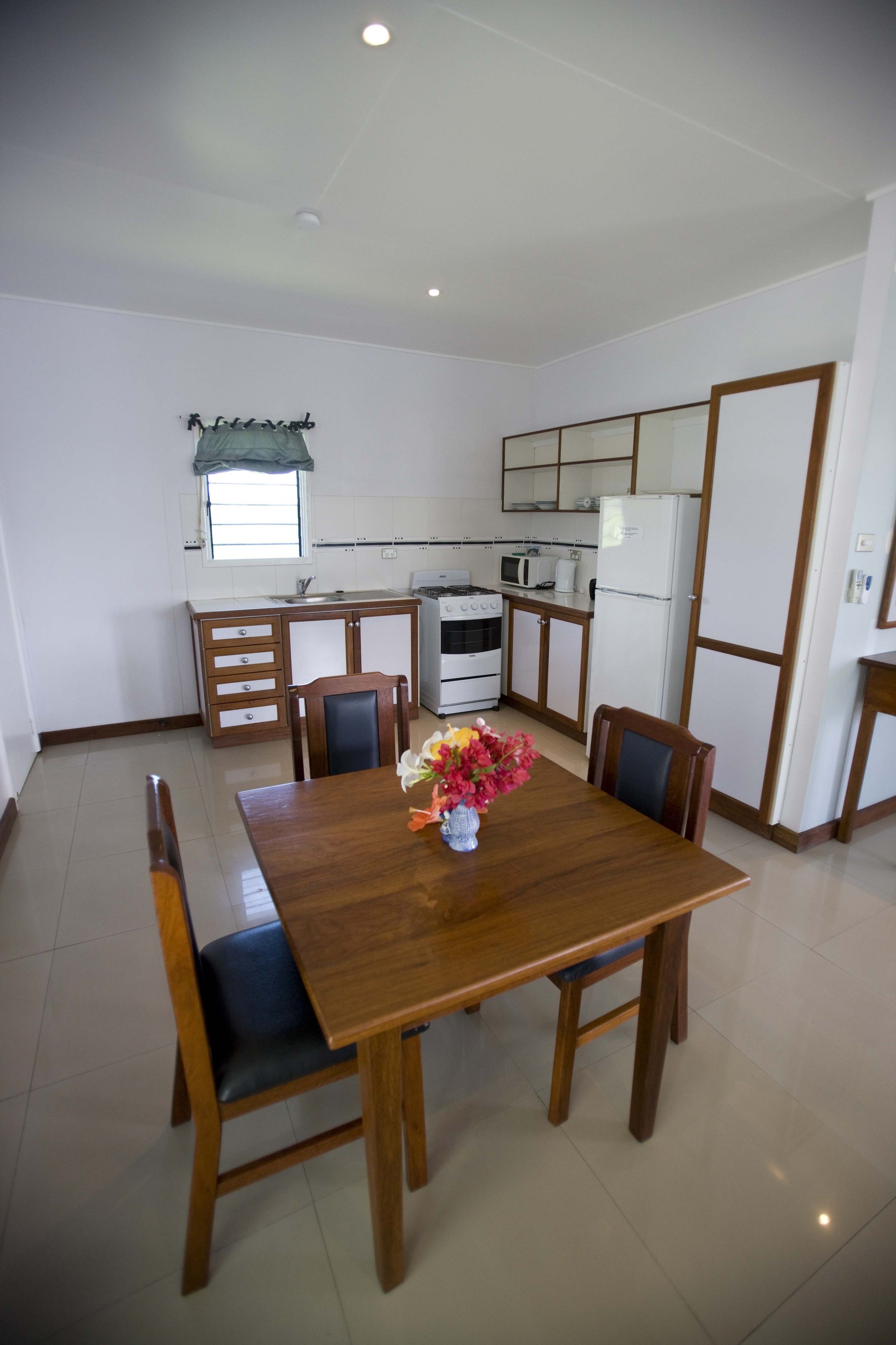 A dining area with a wooden table and chairs, a vase with flowers, and a kitchen in the background.