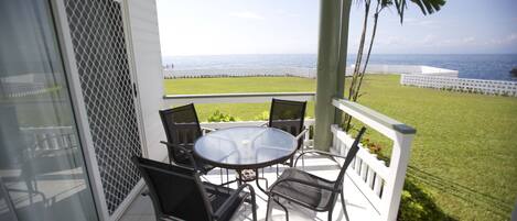 A covered patio with a glass door, a round table with four chairs, and a view of the ocean.