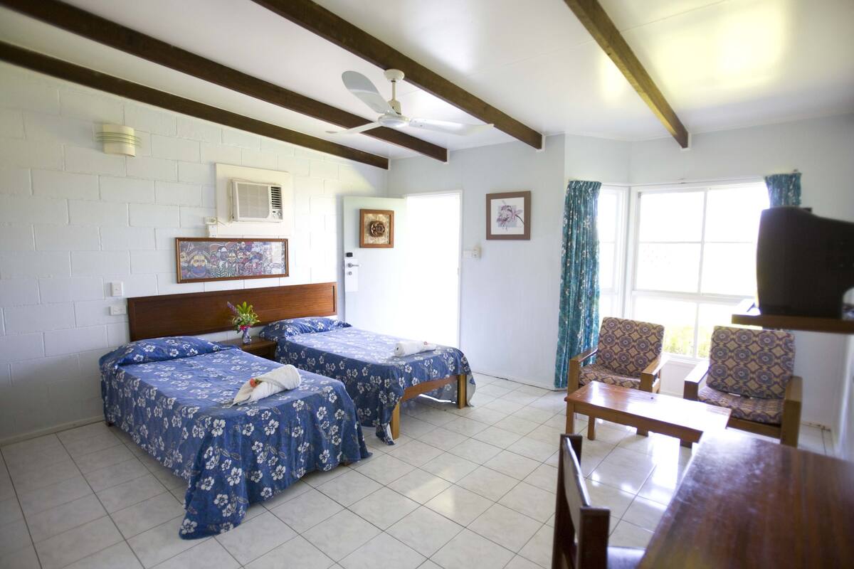 A room with two beds, a ceiling fan, a TV, and a window with curtains.