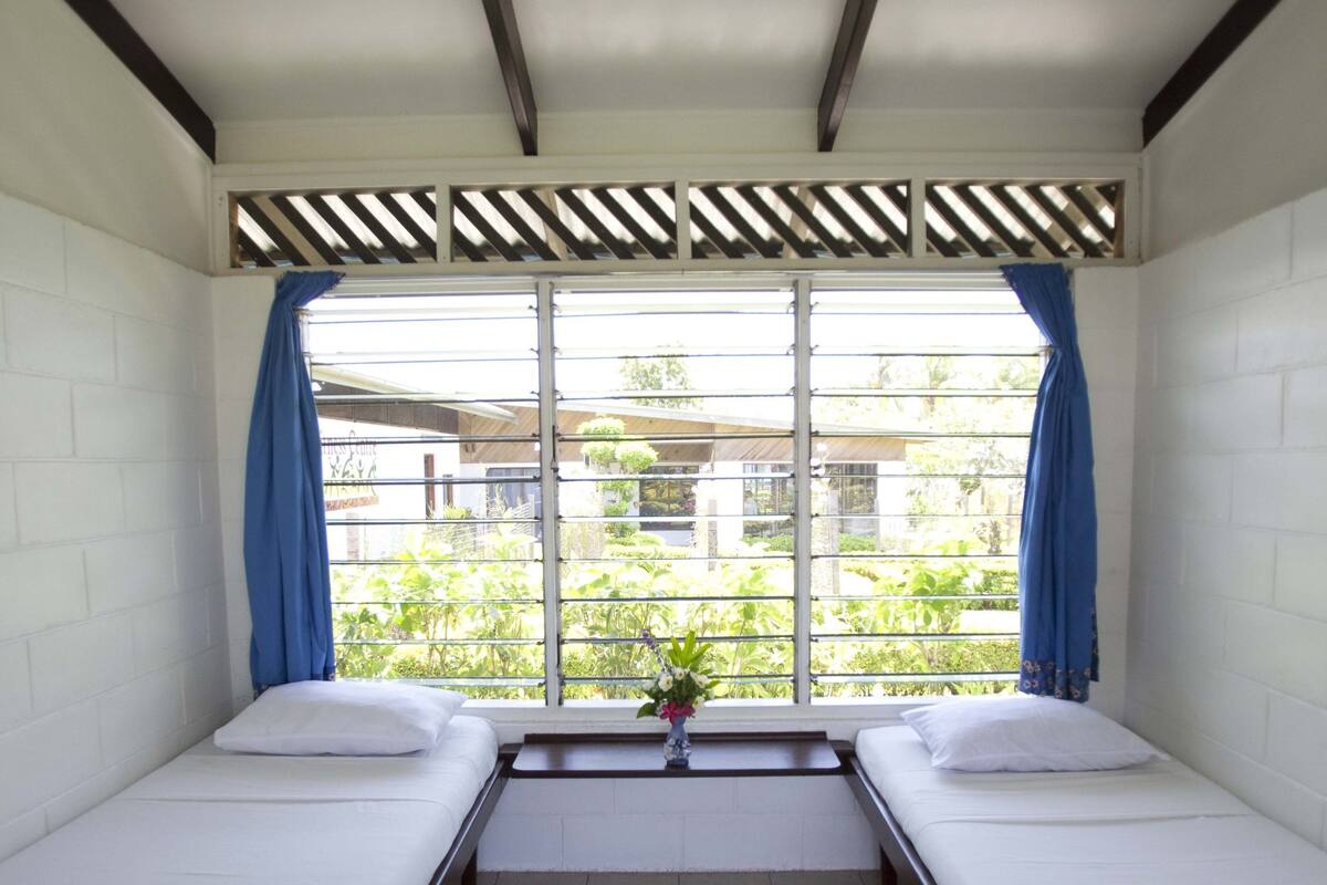 A room with two single beds, a ceiling fan, and a window with blue curtains.