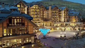 A multi-story hotel with a central courtyard, stone facade, and a ski slope in the background.