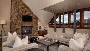 A modern living room with a stone fireplace, a large window with curtains, and a cozy seating area.