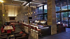 A modern restaurant with a bar area, stone walls, and large windows offering a view of the outdoors.