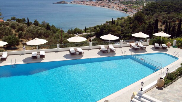 A swimming pool with lounge chairs and umbrellas, surrounded by a scenic view of the sea and hills. - Kalidon Panorama (Samos)