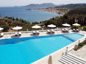 Ein Swimmingpool mit Liegestühlen und Sonnenschirmen, umgeben von einer schönen Aussicht auf das Meer und die Hügel.