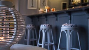 A bar area with a round table, white bar stools, and a hanging light fixture. - Kalidon Panorama (Samos)