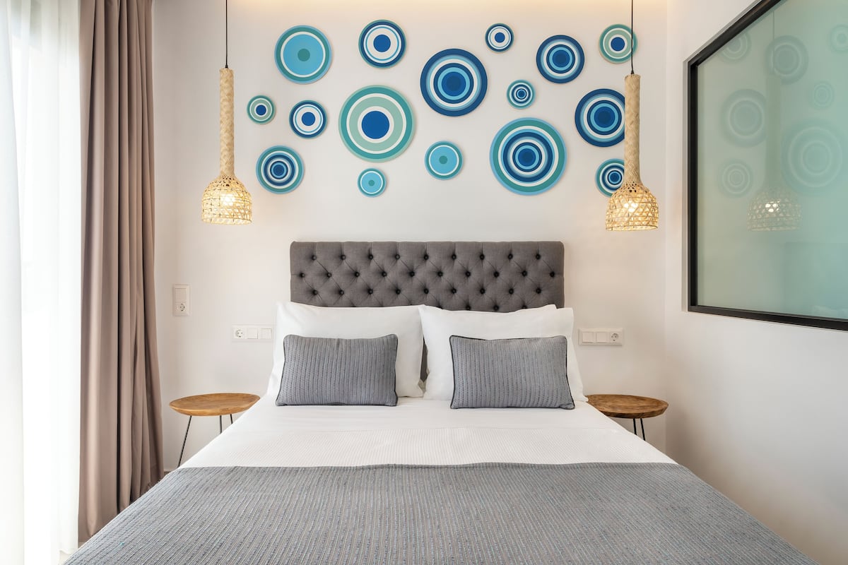 Quarto bem arrumado com cabeceira estofada, duas mesas de cabeceira e uma cama grande com roupa de cama cinzenta.
