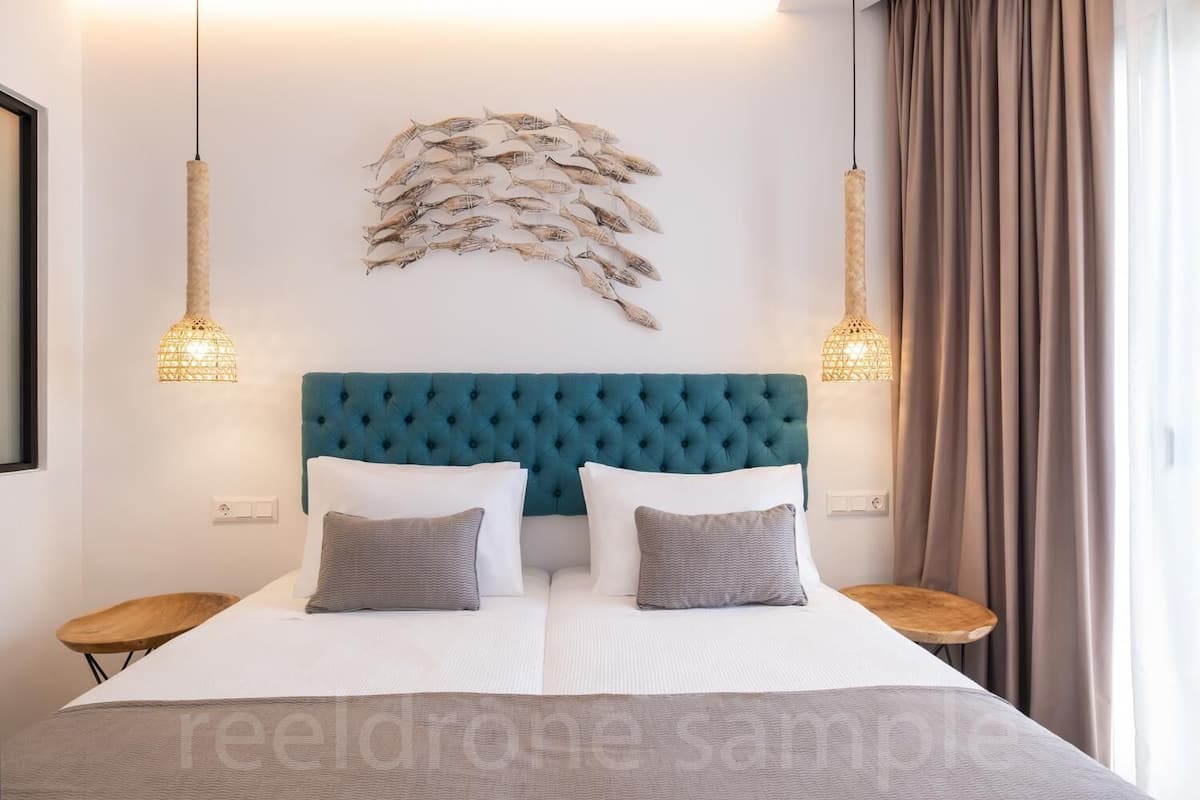 Quarto com cabeceira acolchoada em tons de verde-água, duas mesas de cabeceira, uma cama grande com roupa de cama branca e um objeto decorativo na parede acima da cama.