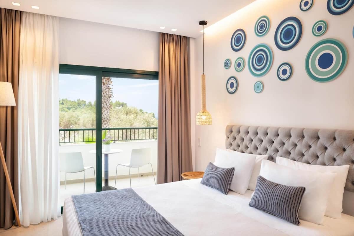 Quarto de hotel com uma cama grande, vista para o verde pela janela e parede decorativa com padrões circulares.