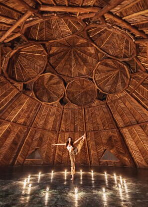 A person standing in a room with a thatched roof and multiple candles on the floor.