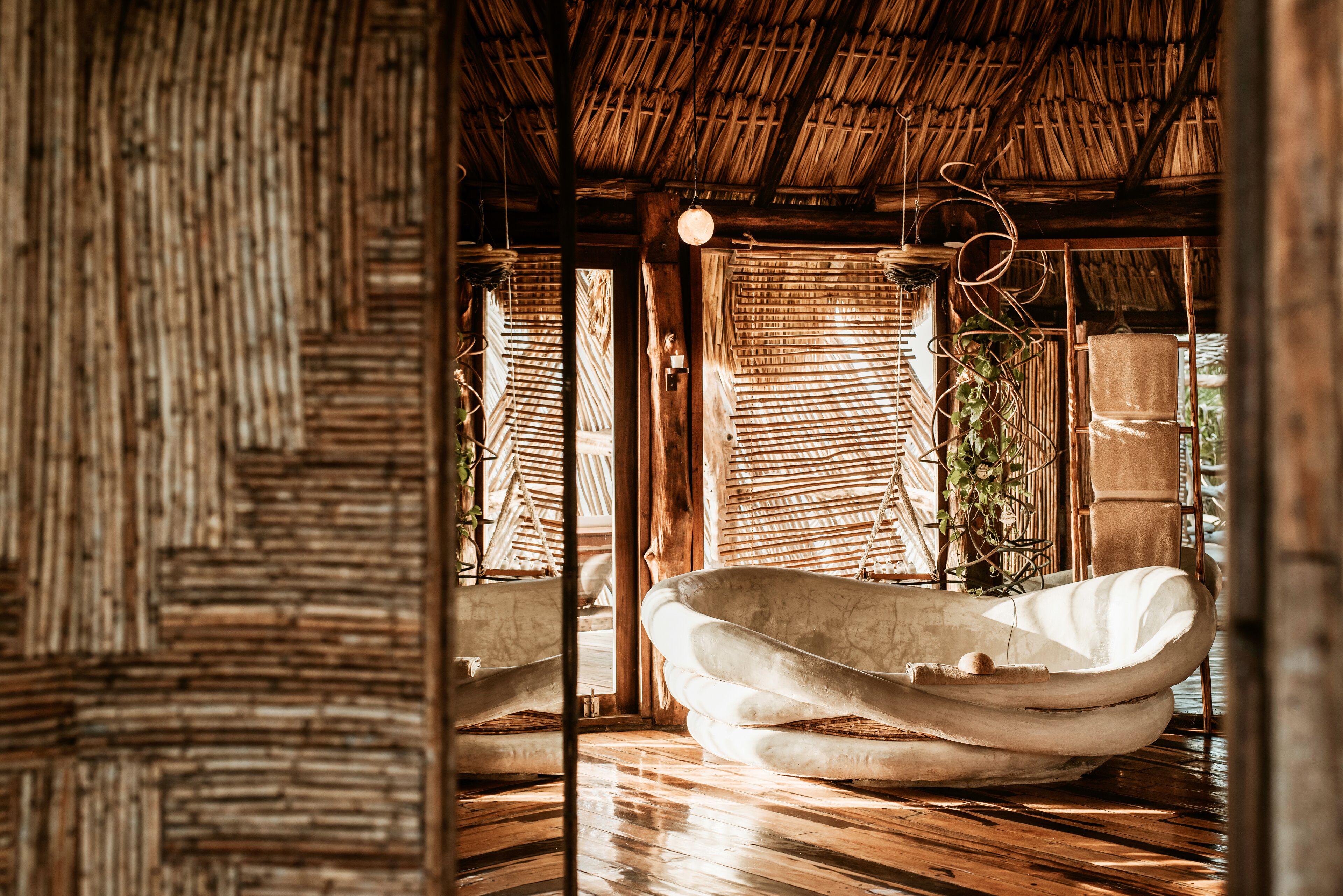 A room with a thatched roof, a hanging light fixture, and a large white bathtub.