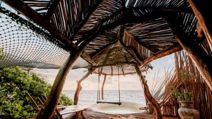 Un espace extérieur aménagé avec une toiture de chaume, comprenant des sièges, une balançoire, un jacuzzi et une vue sur la mer.