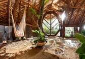 A rustic room with a thatched roof, a hammock, and a large window.