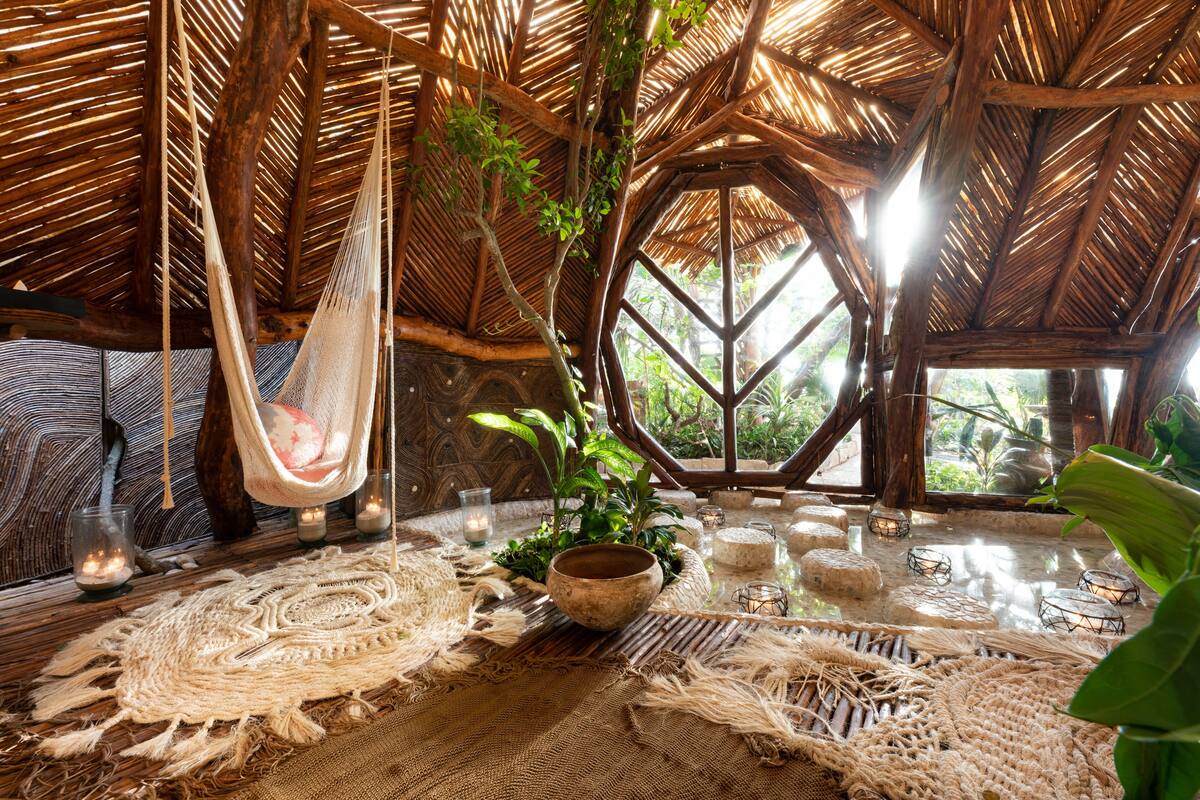 A rustic room with a thatched roof, a hammock, and a large window.