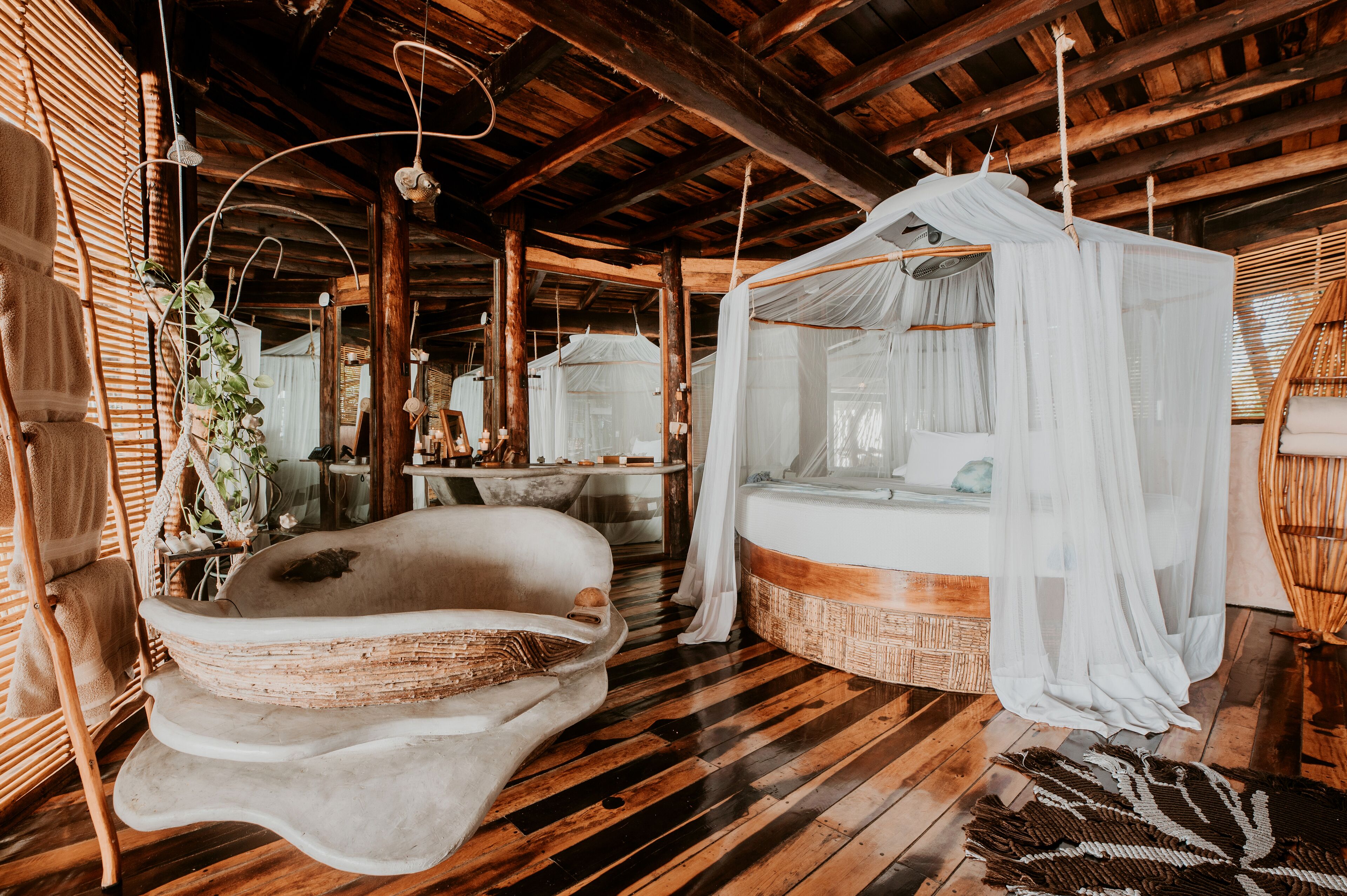 A rustic wooden room with a large bed, a hanging chair, and a unique bathtub design.