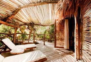 A wooden deck with lounge chairs and a thatched roof structure.