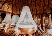A circular wooden bed with a white canopy, wooden floors, and a thatched roof.