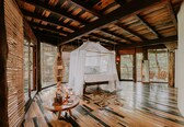 A room with a bed under a canopy, wooden floors, and large windows with blinds.