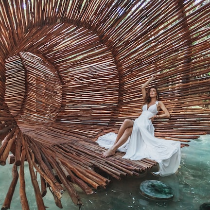 A woman sitting on a curved bamboo structure in a natural setting.