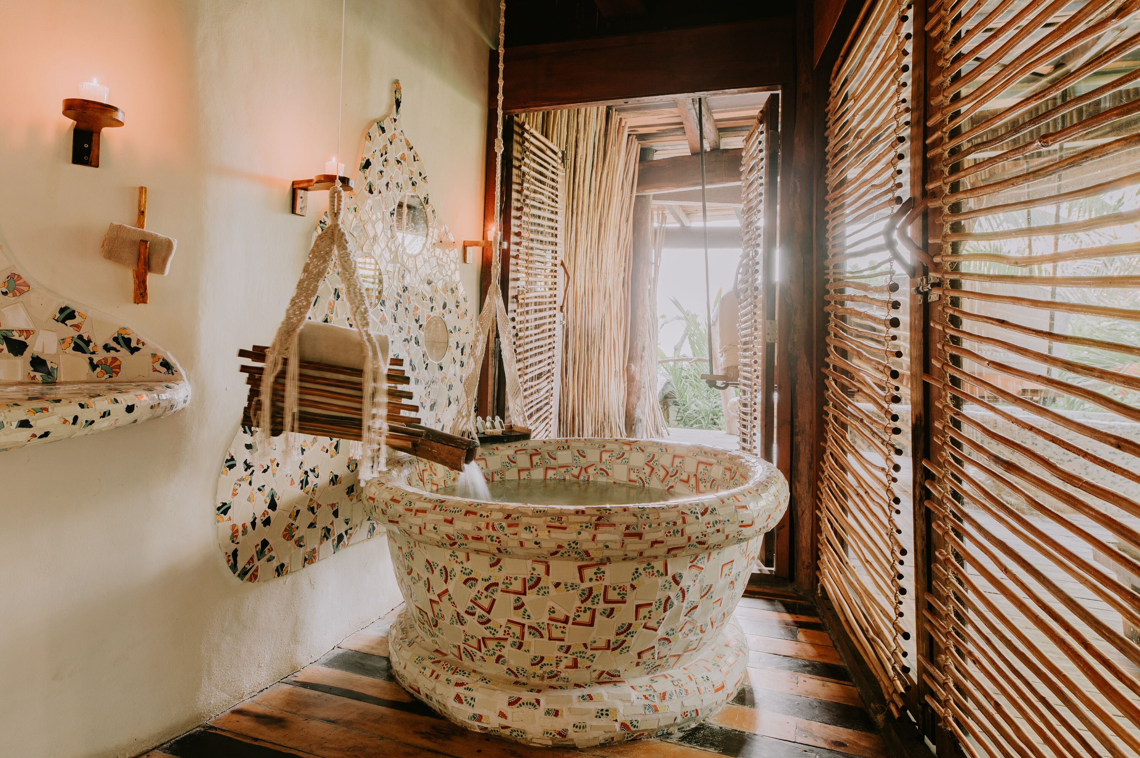 A traditional bathtub with a patterned design, a wooden shelf with a towel, and a wall-mounted light fixture.
