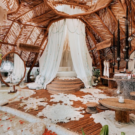 A rustic, thatched-roof room with a canopy bed, woven furniture, and a small garden area.