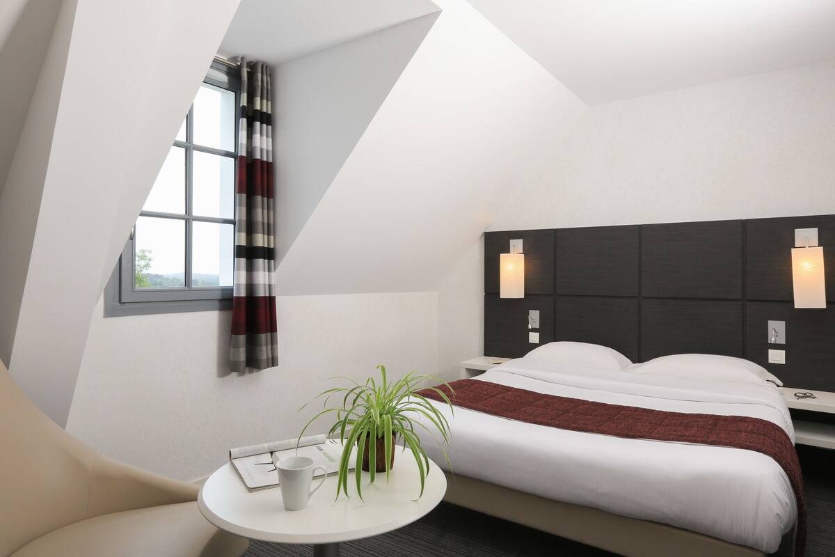A modern hotel room with a bed, bedside table, and a window with curtains.
