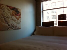 Een hotelkamer met een groot bed, een raam met uitzicht op gebouwen en een schilderij aan de muur.
