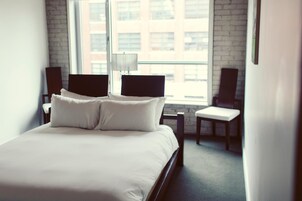 Een moderne hotelkamer met een groot bed, twee stoelen, een lamp en uitzicht op de stad door het raam.