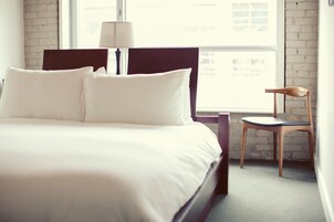 Een net opgemaakt bed met witte lakens in een kamer met zichtbare bakstenen muren en een groot raam.