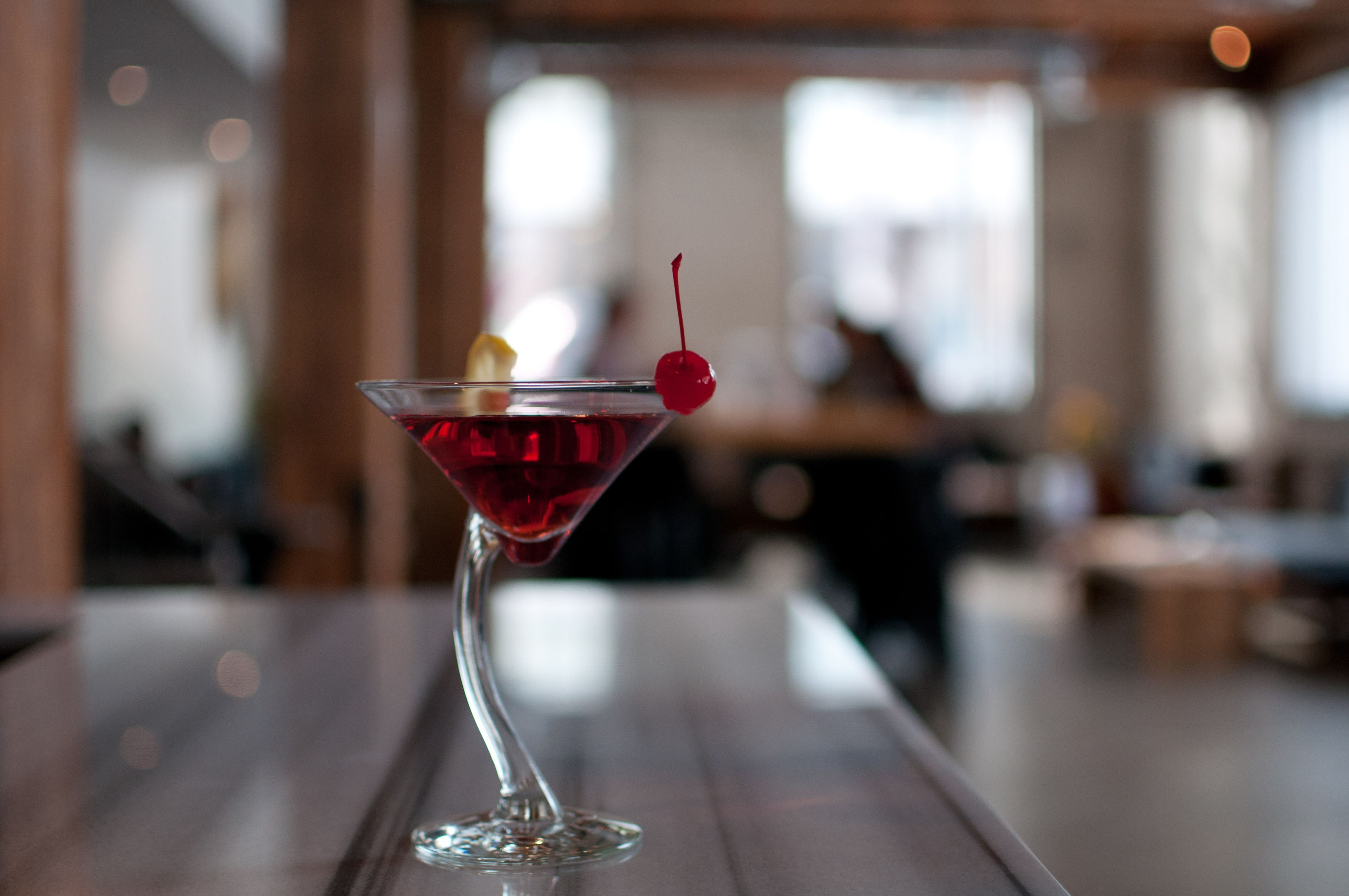A martini glass with a cherry on a wooden bar counter.