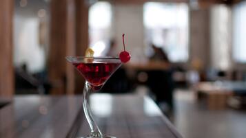 A martini glass with a cherry on a wooden bar counter.