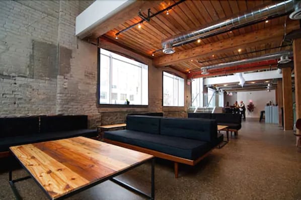 A spacious lounge with wooden tables and dark sofas, large windows, and exposed ductwork on the ceiling. - Hotel Ocho (Toronto)