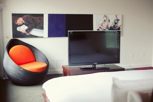 Een moderne hotelkamer met een groot flatscreen televisietoestel, een opvallende oranje fauteuil en kunst aan de muur.