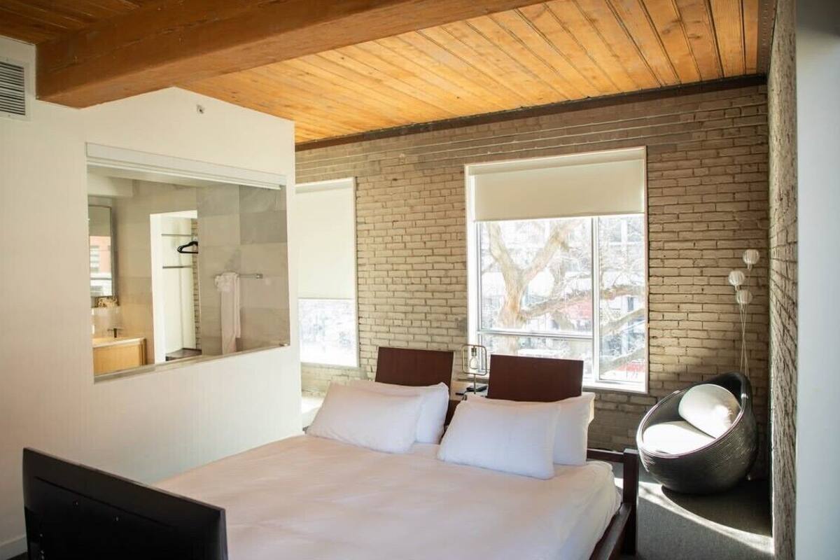 Une chambre moderne avec un grand lit, un plafond en bois, un mur en briques et une fenêtre.