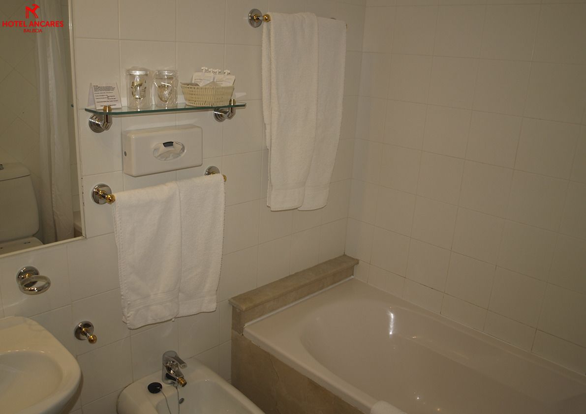 Un baño con bañera, lavamanos, espejo y estantes con artículos de aseo.