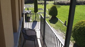 A balcony with a chair and a table, overlooking a green landscape with trees and a stone wall. - Hotel Ancares (Balboa)