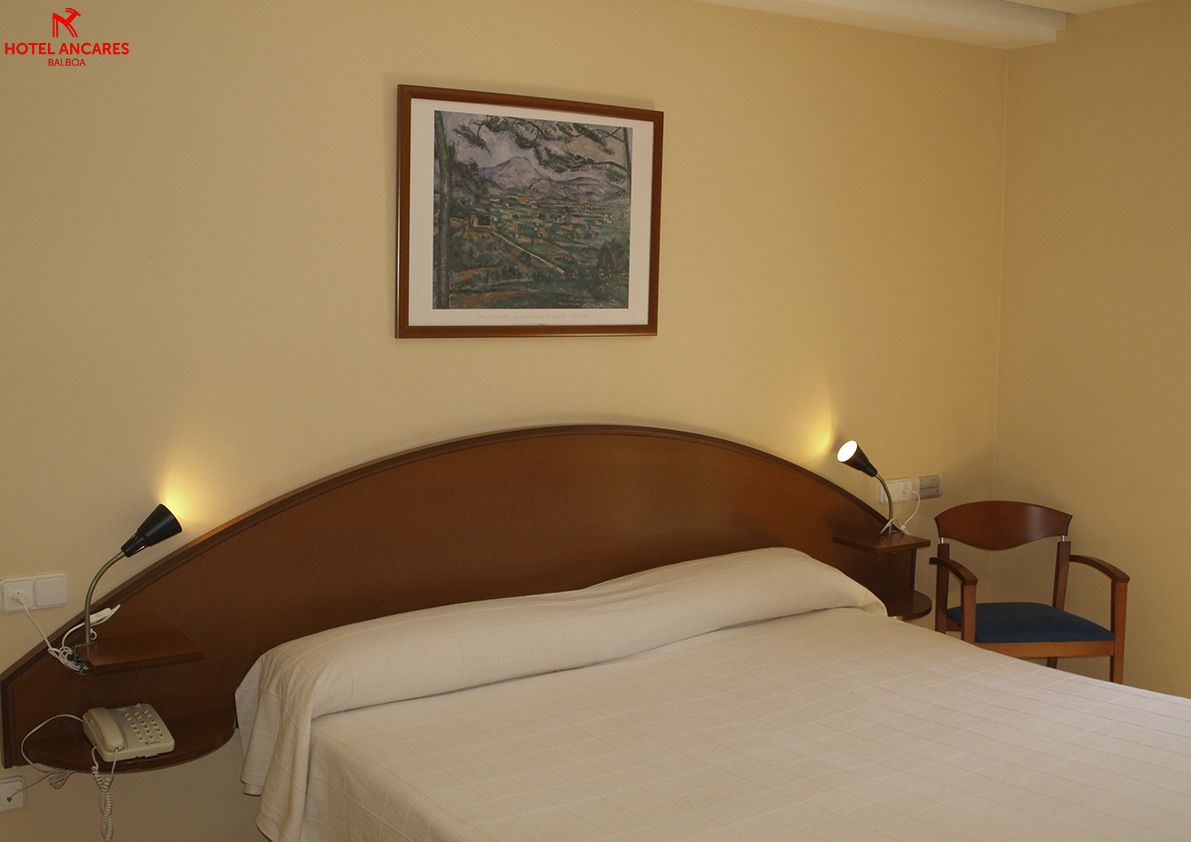 Una habitación de hotel con cama, lámpara de noche, sillón y un cuadro en la pared.