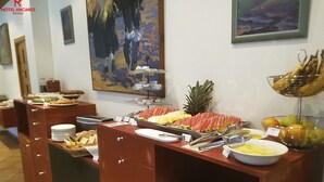 A buffet setup with various food items, including fruits and vegetables, arranged on a counter with a painting in the background. - Hotel Ancares (Balboa)