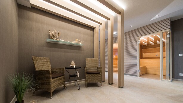 A modern lobby with wicker chairs, a small table, and a shelf with decorative items. - Hotel Muschelgrund (Cuxhaven)