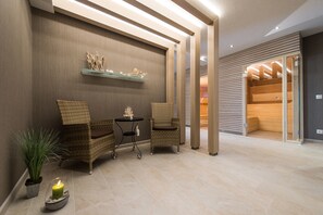 A modern lobby with wicker chairs, a small table, and a shelf with decorative items. - Hotel Muschelgrund (Cuxhaven)