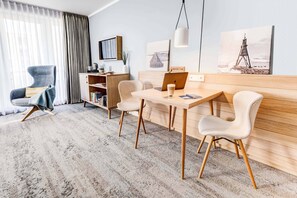A modern hotel room with a wooden desk, two chairs, a laptop, and a bookshelf.