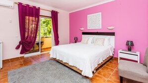 Un dormitorio con cama, mesita de noche, silla y vista a través de un ventanal corredero.