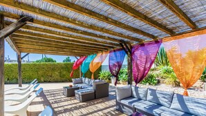 Un patio exterior con mobiliario de mimbre, una pérgola con toldo a rayas y un seto bien cuidado al fondo.