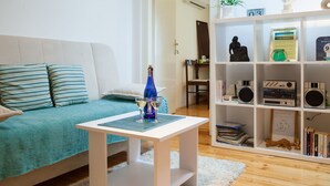 Un salon avec un canapé de couleur turquoise, une table basse blanche et une bibliothèque contenant divers objets.