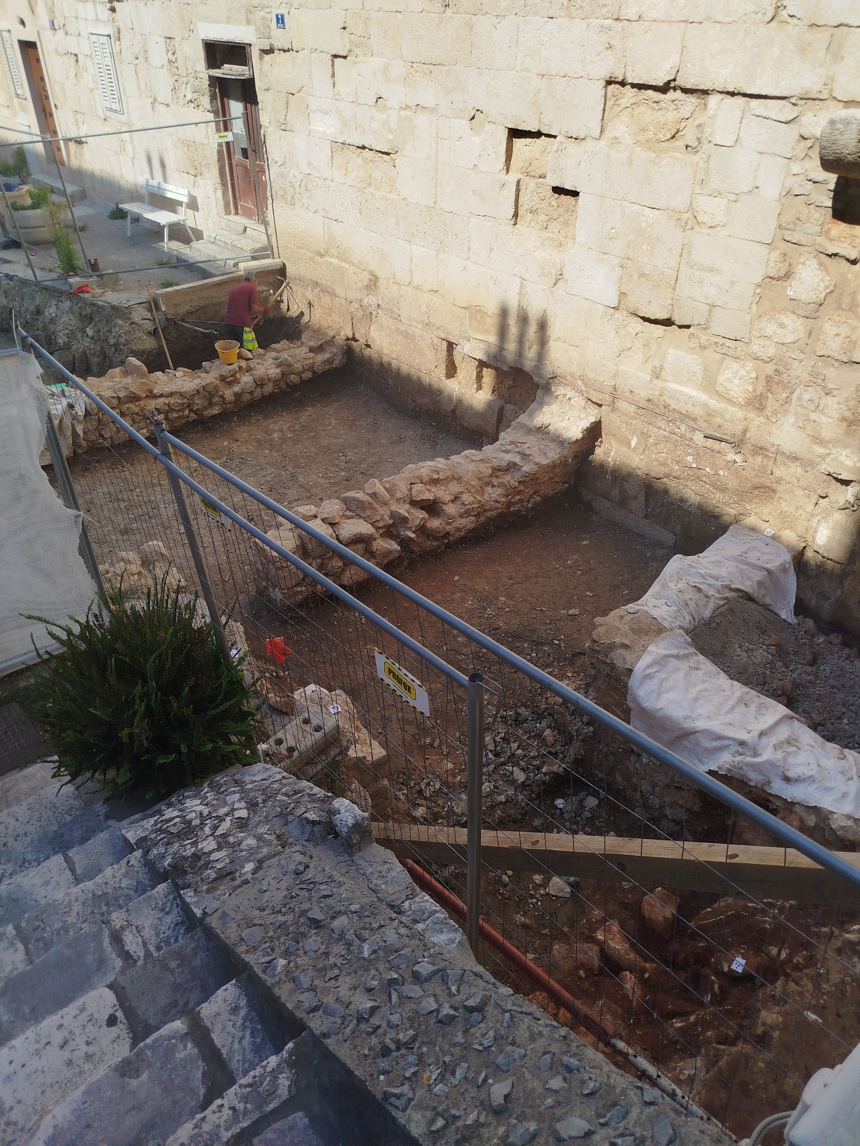Un sitio de construcción con una estructura en construcción, una cerca metálica y una banca pequeña.