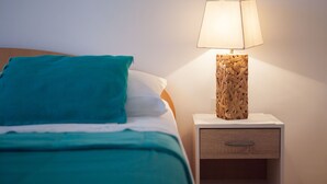 Un lit bien fait, avec une literie de couleur turquoise, un oreiller blanc et une table de chevet en bois dotée d’un tiroir.
