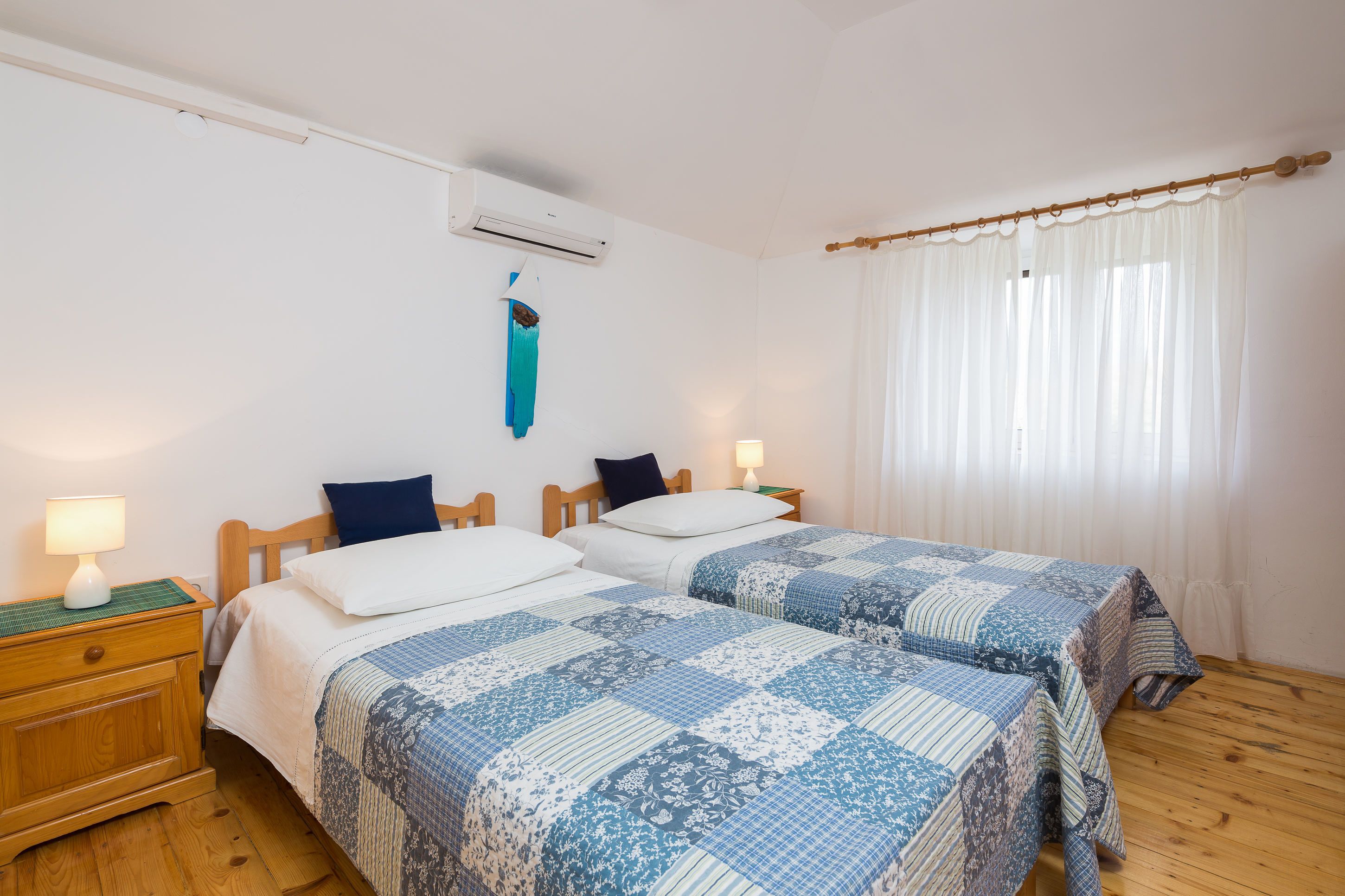 A bedroom with two beds, a wooden headboard, a hanging towel, and a window with curtains.