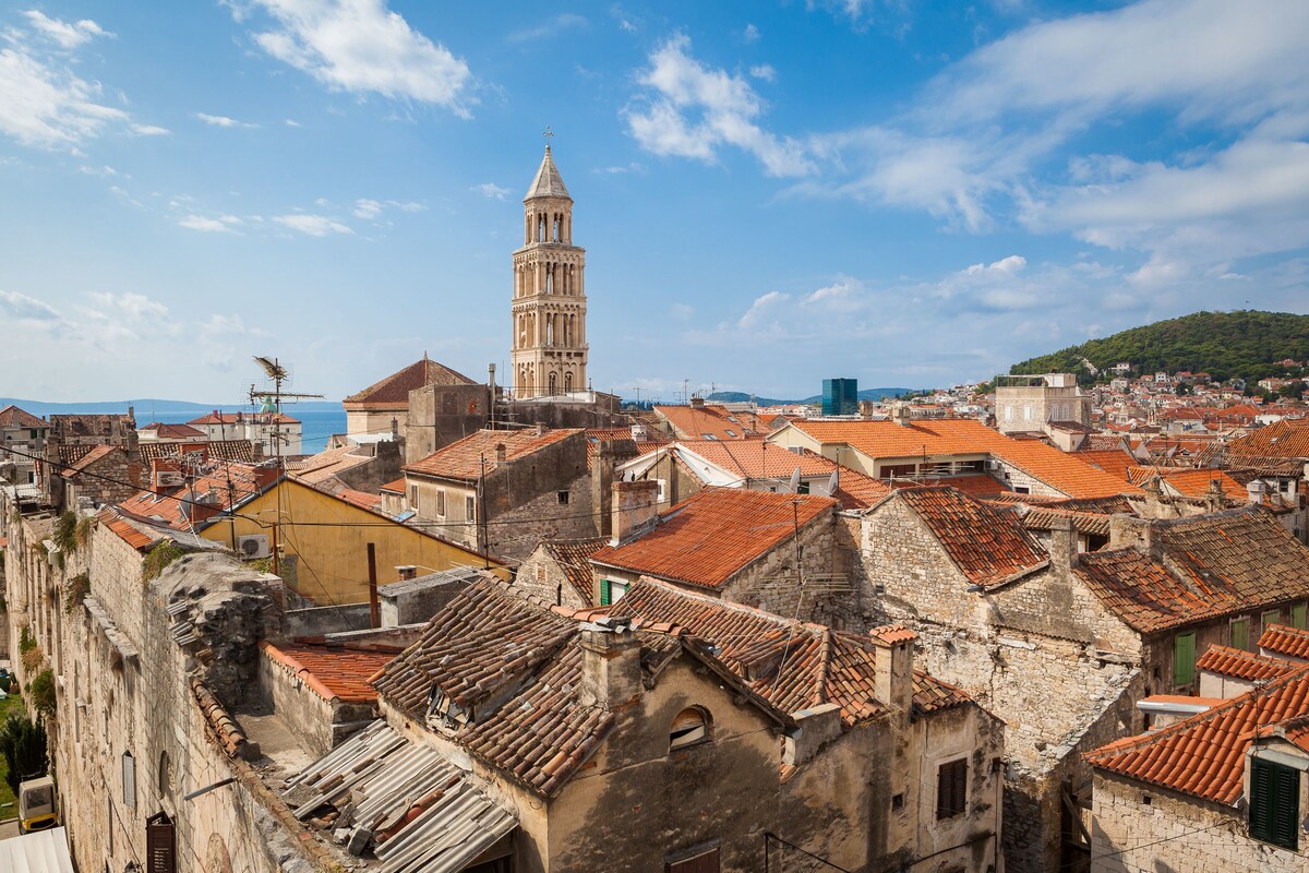 A historic town with a prominent tower, terracotta-roofed buildings, and a view of the sea.
